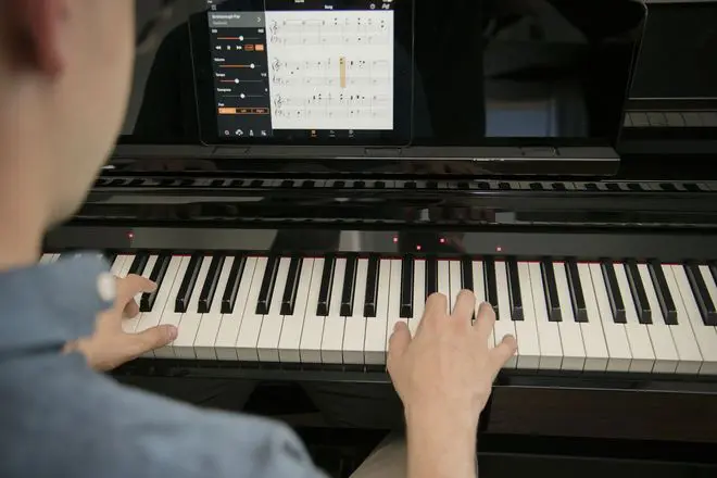 Person playing a Yamaha Clavinova CSP-255 smart piano with lighted keys and sheet music on a tablet